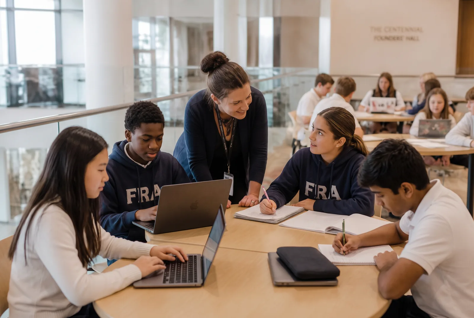 Students working together at a table in an independent school learning commons while a teacher leans in to guide them