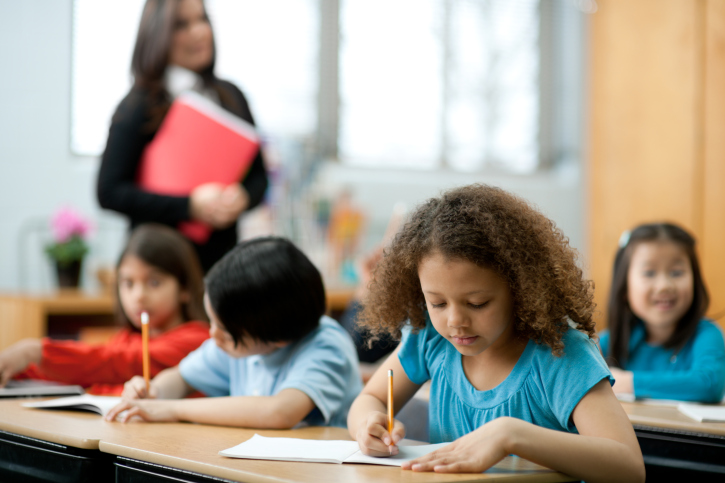 Diverse elementary students writing at their desks in a classroom
